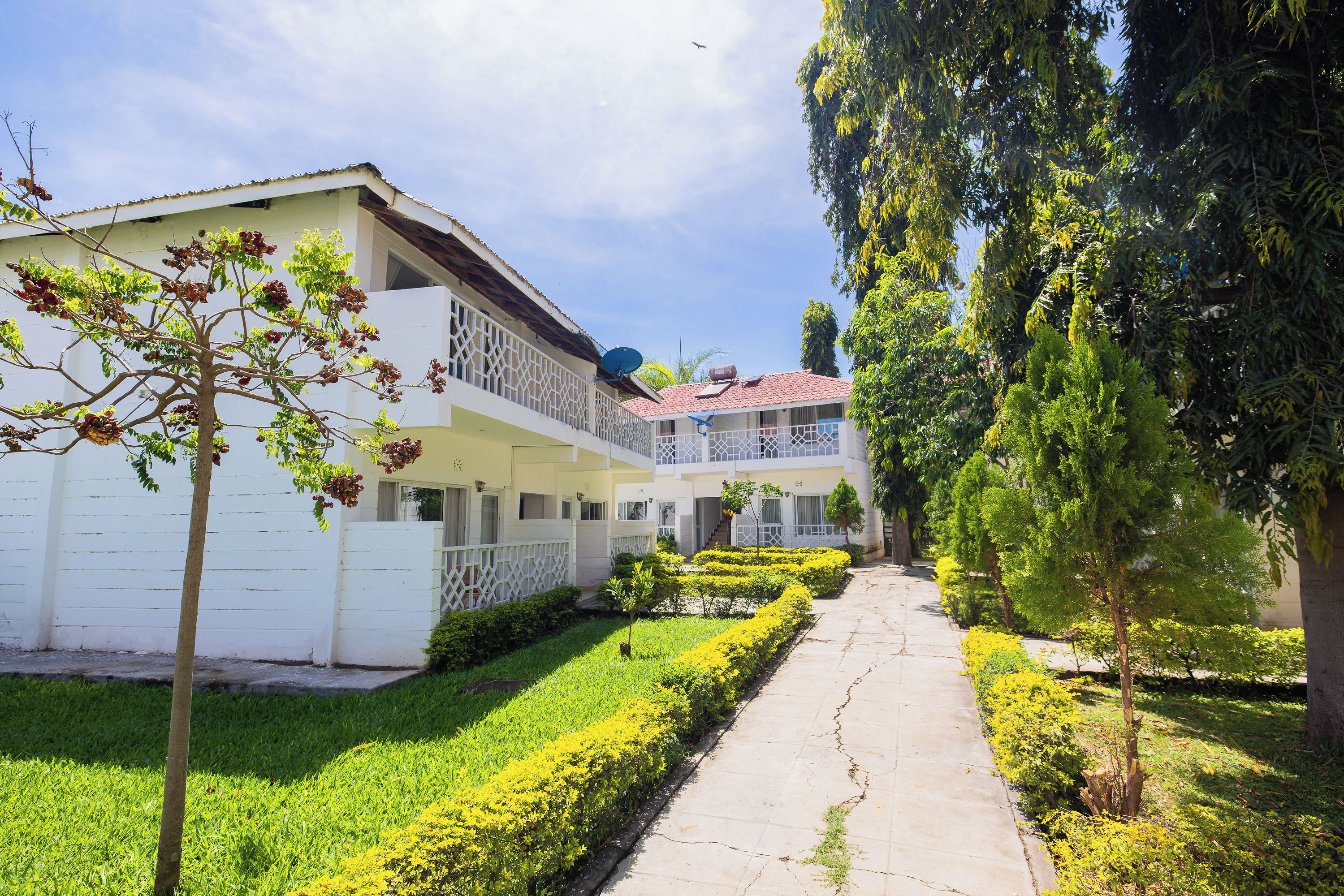 A two-story building with a balcony, a satellite dish, and a well-maintained garden with a pathway.