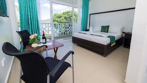 A hotel room with a bed, a table with a chair, a window with curtains, and a view of the outdoors. - Mbita Tourist Hotel (Mbita)