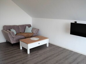 A living room with a grey sofa, a wooden coffee table, and a flat-screen TV mounted on the wall. - House No. 25, Holiday Home Fischerhus (Wangerland)