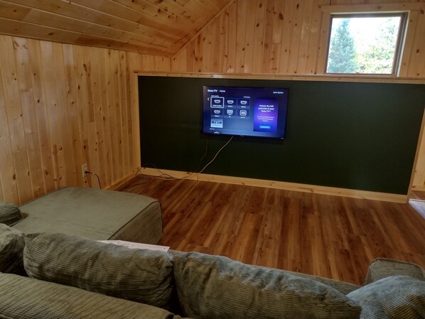 A room with a flat-screen TV mounted on a wall, wooden flooring, and a green couch.