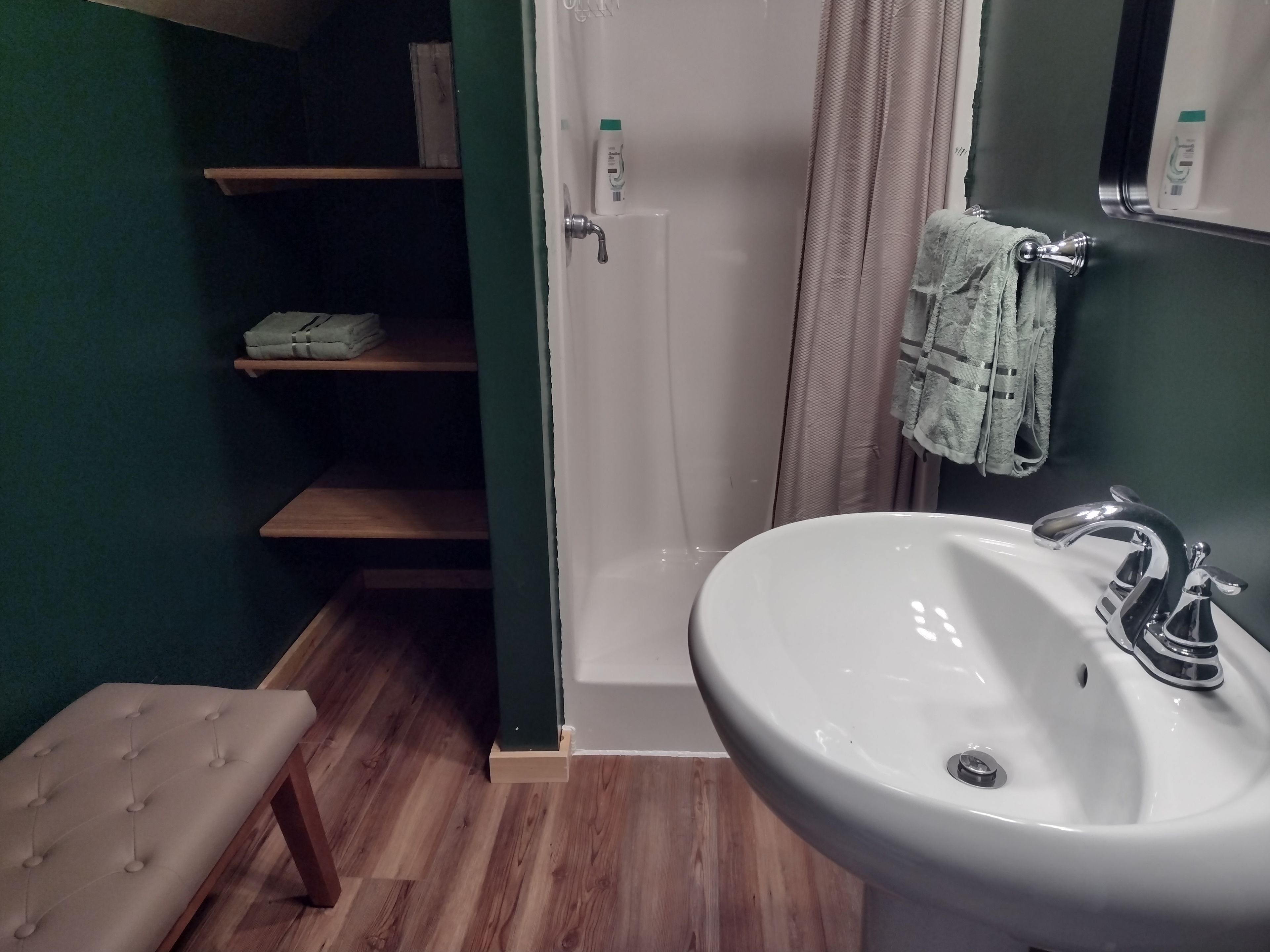 A bathroom with a white sink, a shower curtain, and a bench.