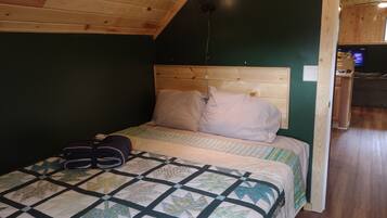 A bedroom with a wooden ceiling, a bed with a quilt, pillows, and a pair of shoes on the floor.