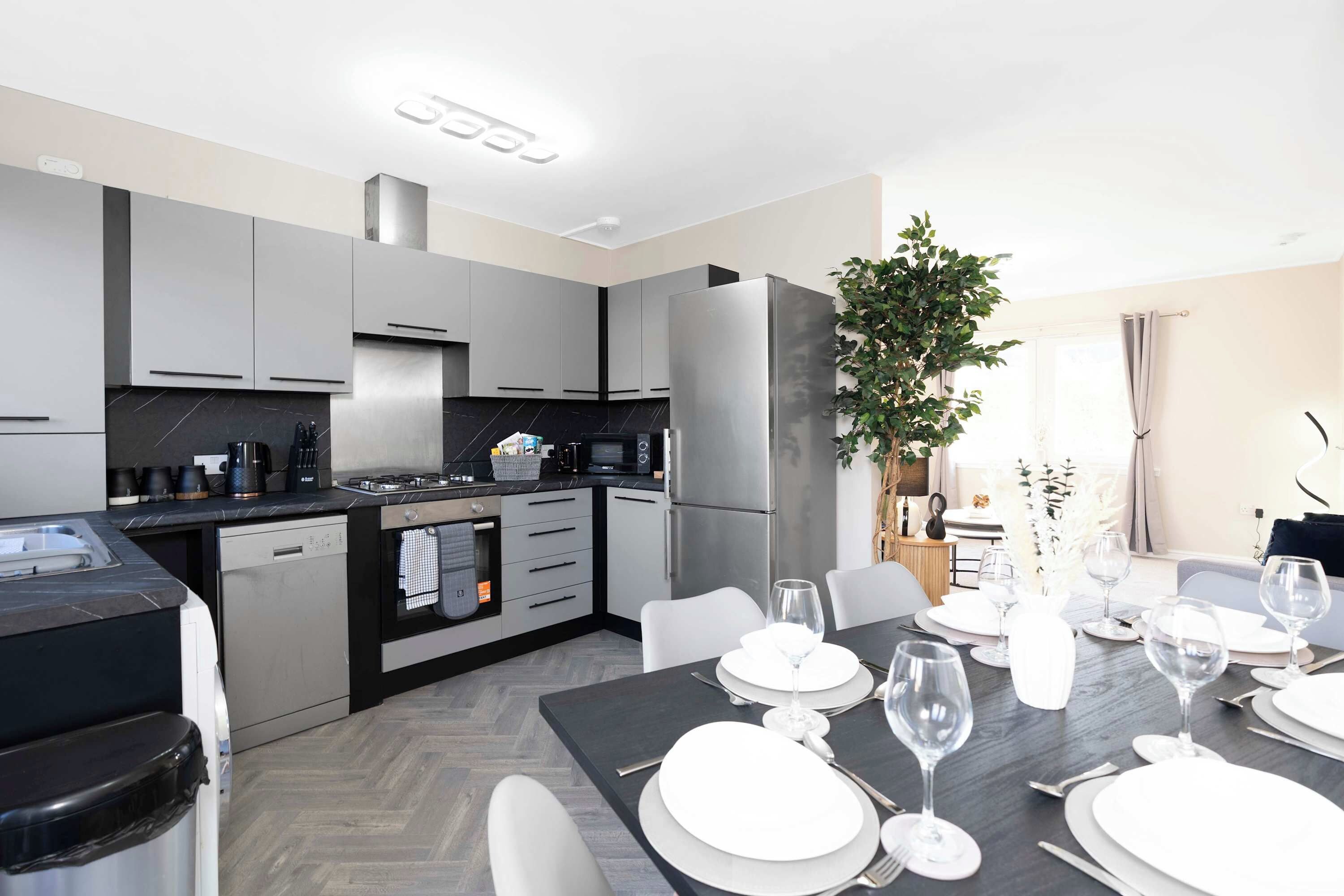 A modern kitchen with grey cabinets, a built-in oven, and a dining area set for a meal with white plates and wine glasses.