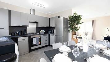 A modern kitchen with grey cabinets, a built-in oven, and a dining area set for a meal with white plates and wine glasses.
