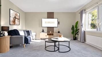 A modern living room with a sofa, a coffee table, a TV, and a window with curtains.
