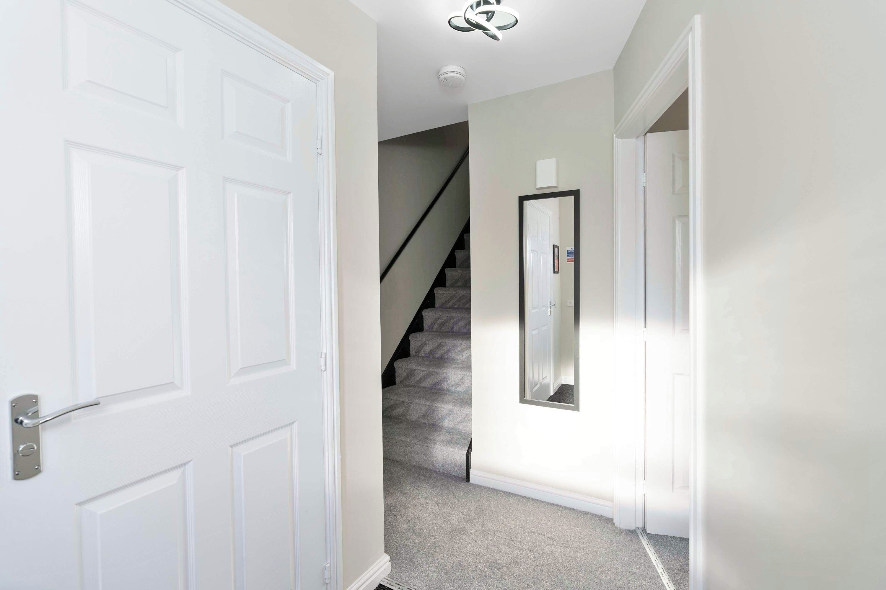 A hallway with a white door, a staircase, and a wall-mounted mirror.