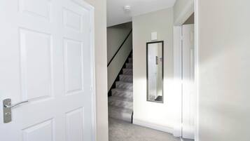A hallway with a white door, a staircase, and a wall-mounted mirror.