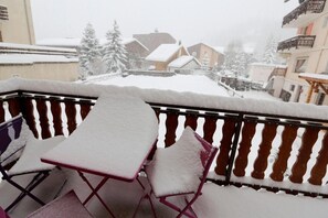 Ein mit Schnee bedeckter Balkon mit Tisch und Stühlen mit Blick auf eine verschneite Wohngegend.