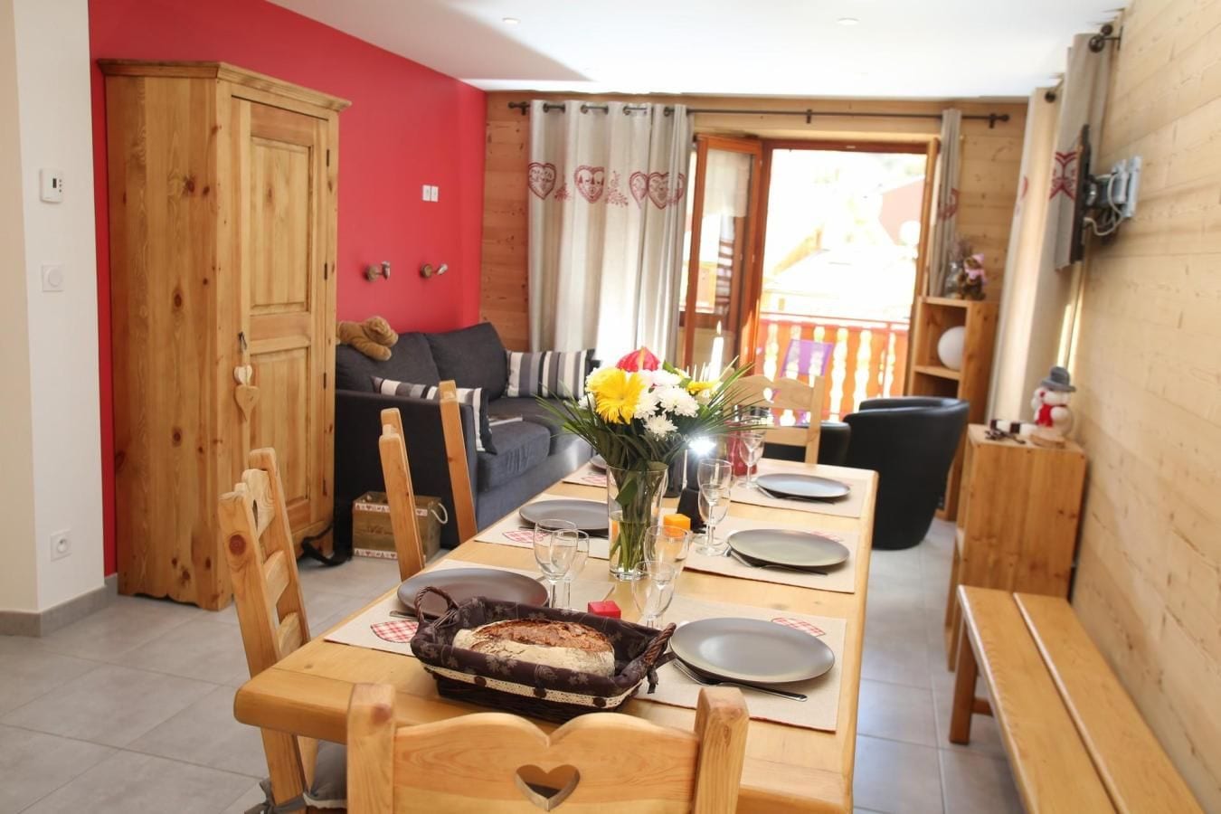 Un coin repas avec une table en bois dressée pour deux personnes, un vase rempli de fleurs et une pizza posée sur la table.
