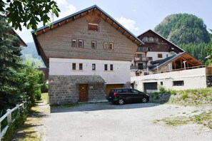 Ein zweistöckiges Holzgebäude mit Steineingang, ein Auto davor und eine Bergkulisse.