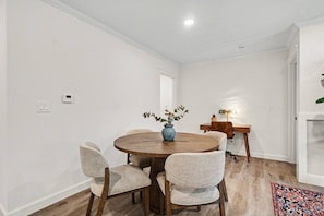A dining area with a round table, four chairs, a vase with flowers, a lamp, and a wooden desk with a chair. - New 4BR Home | Ideal for Families & Teams (Dayton)