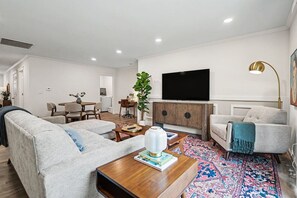 Un salon moderne comprenant un canapé, un fauteuil, une table basse et un téléviseur fixé au mur.