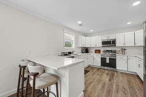 A modern kitchen with white cabinetry, a central island, and a bar stool area. - West Dayton New 4BR/3BA Home | Modern & Spacious (Dayton)