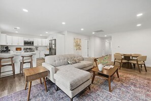 A modern living room with a grey sofa, wooden coffee table, and a dining area with a wooden table and chairs. - West Dayton New 4BR/3BA Home | Modern & Spacious (Dayton)