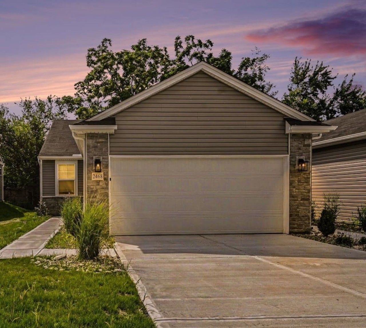 Un garage attenant à une maison, avec le numéro « 2468 » sur la porte, une allée et une maison dont le toit est en pente.