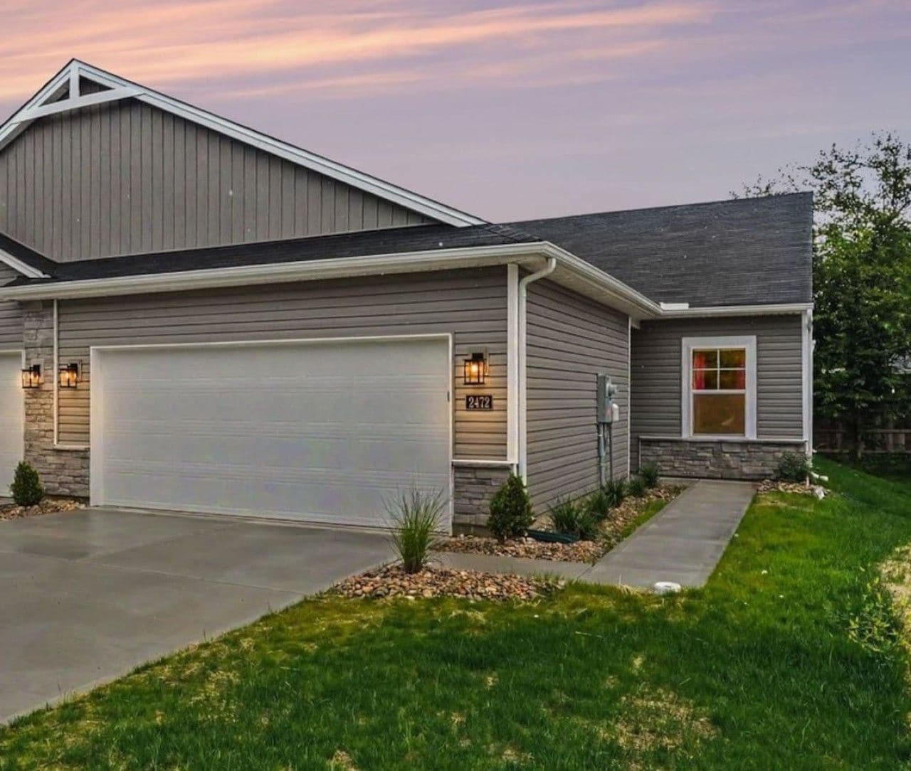 Une maison à deux étages avec un garage, une porte d’entrée et un petit jardin devant, avec un chemin.