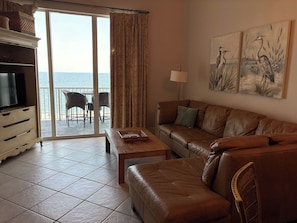 Ein Wohnzimmer mit einer Couch, einem Fernseher, einem Couchtisch und einem Balkon mit Sitzgelegenheiten.