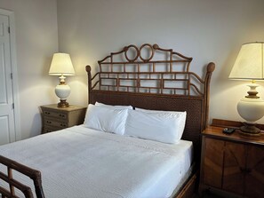 Ein ordentlich bezogenes Bett mit weißen Leinen, ein Holzkopfstück mit Gittermuster und zwei Nachttische mit Holz, jeweils mit einer Nachttischlampe.