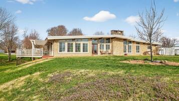 A two-story stone house with a covered porch, a fenced deck, and a well-maintained lawn.