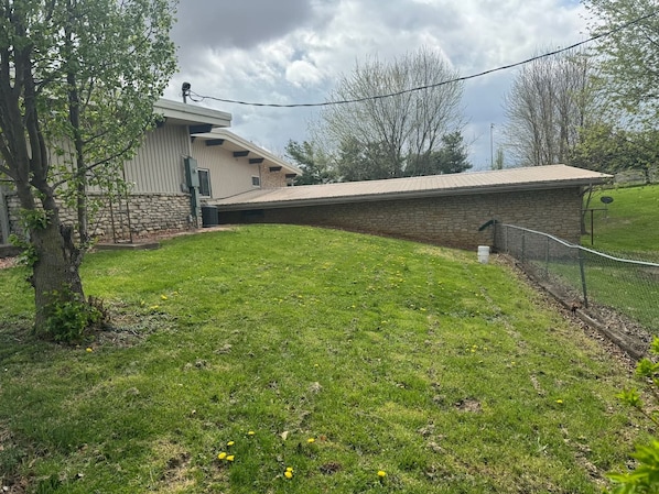 A grassy yard with a stone wall and a building with a sloped roof.