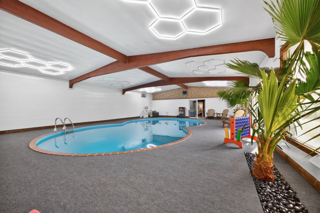 Ein Innenpool mit sechseckiger Deckenkonstruktion, eine kleine Liegefläche am Pool und eine Zimmerpflanze.