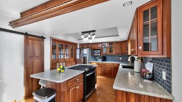 A kitchen with wooden cabinets, a central island, stainless steel appliances, and a black trash bin.