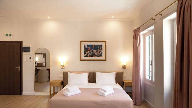 Une chambre d’hôtel avec un lit, deux tables de chevet, un tableau au mur et une porte portant un panneau indiquant la sortie de secours.
