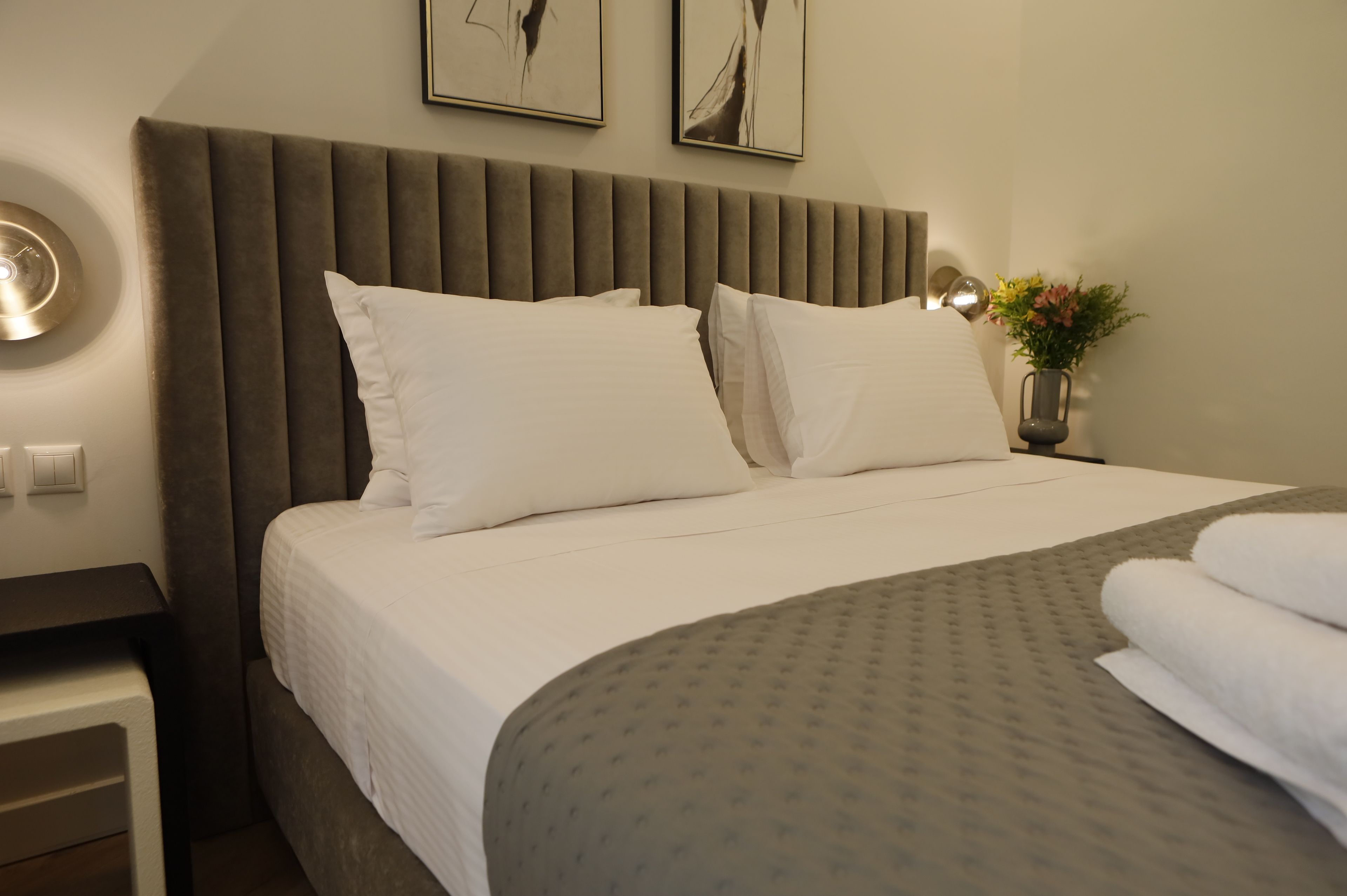 Een netjes opgemaakt bed met witte lakens, een grijs hoofdbord en een grijze, gestreepte plaid.