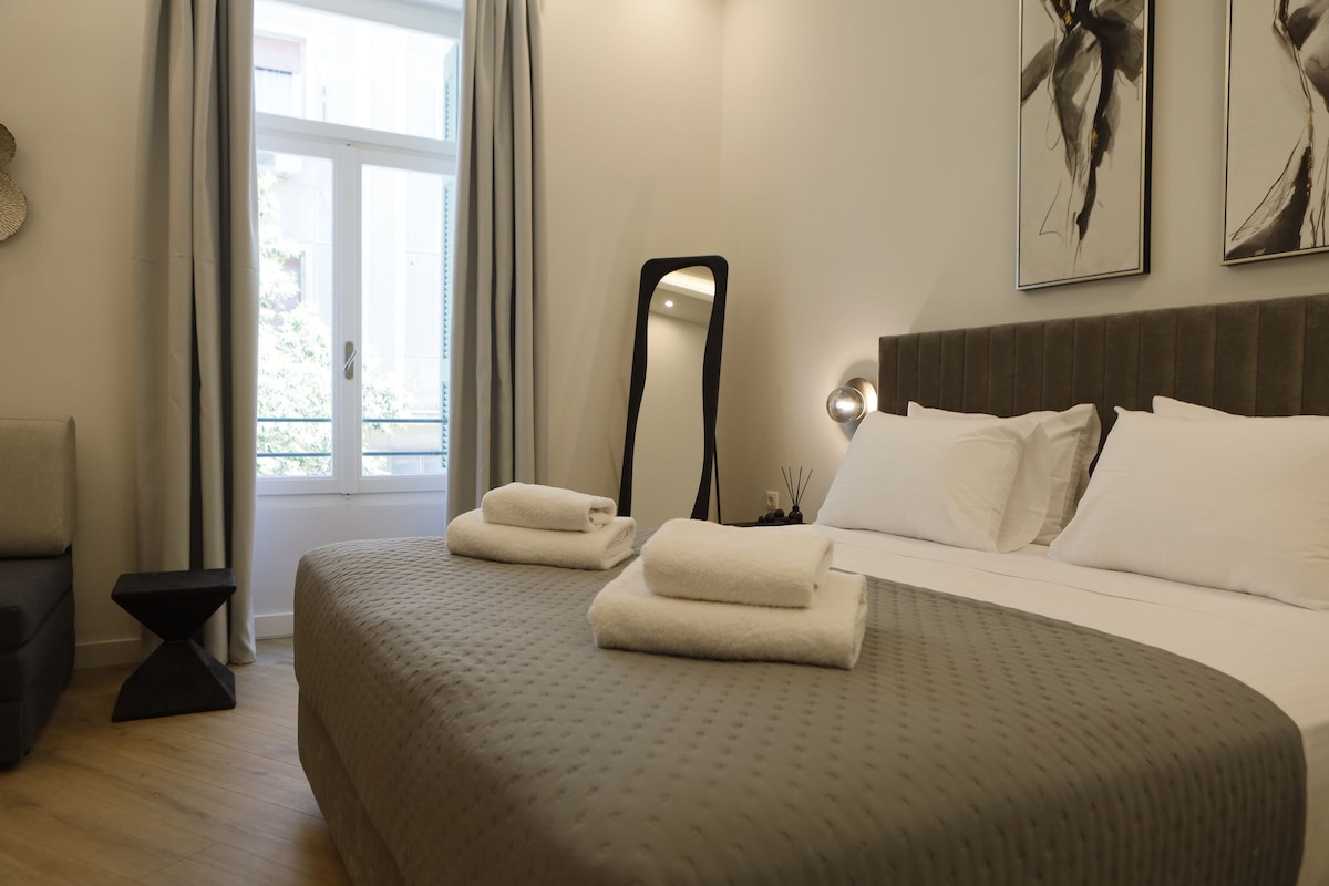 Una habitación de hotel con cama, mesita de noche, espejo y ventana con cortinas.