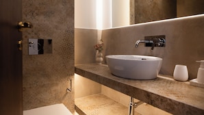 Une salle de bain moderne avec un grand lavabo sur pied, un miroir et un petit vase avec des fleurs posé sur le comptoir.