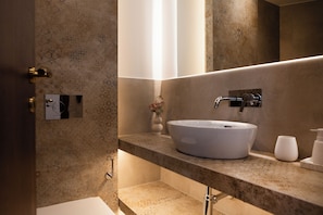 Un baño moderno con un lavamanos de diseño, un espejo y un pequeño florero con flores sobre la encimera.