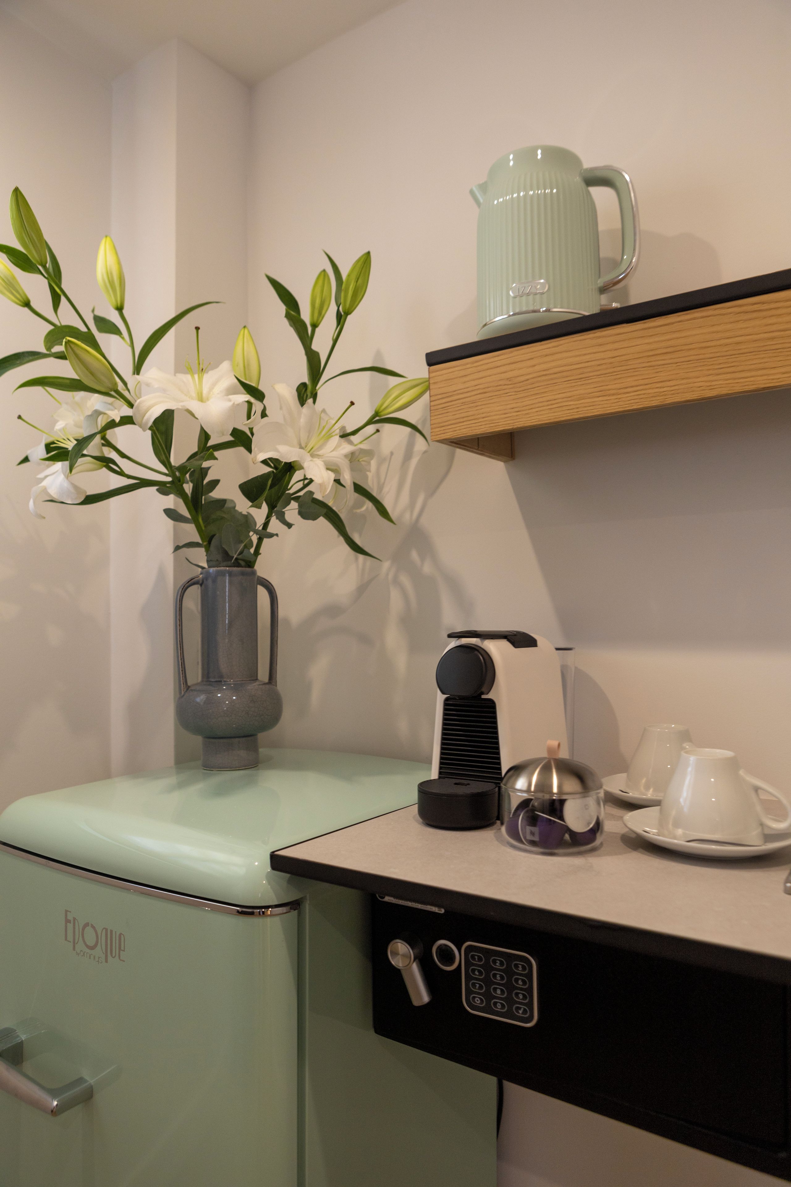 Een compact keukenhoekje met een vintage koelkast, een koffiezetapparaat, een waterkoker en een klein plankje met een karaf.