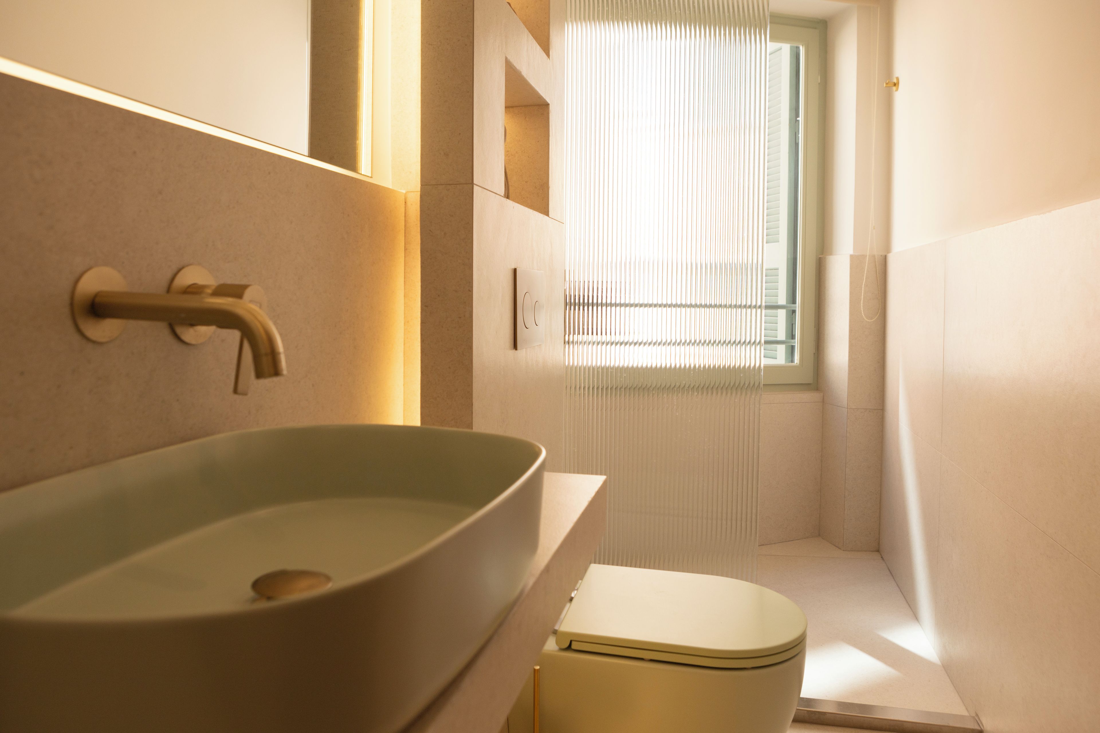 Un baño con lavamanos sobre encimera, inodoro y ventana con persianas.