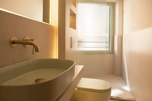 Un baño con lavamanos sobre encimera, inodoro y ventana con persianas.