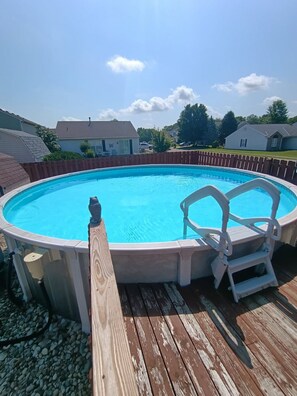 En cirkulær overjordisk swimmingpool med en træterrasse og en stige, omgivet af et træhegn.
