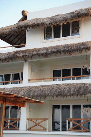 A multi-story building with thatched roofs and wooden railings. - Pacific Dreams Hotel Suites  (Agua Blanca, Cozoaltepec)