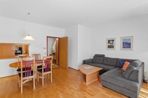 A living room with a grey sofa, wooden dining table with chairs, a small wooden side table, and a pendant light.
