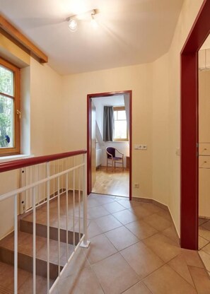 Un pasillo con una escalera que lleva a una habitación con ventana y una silla.