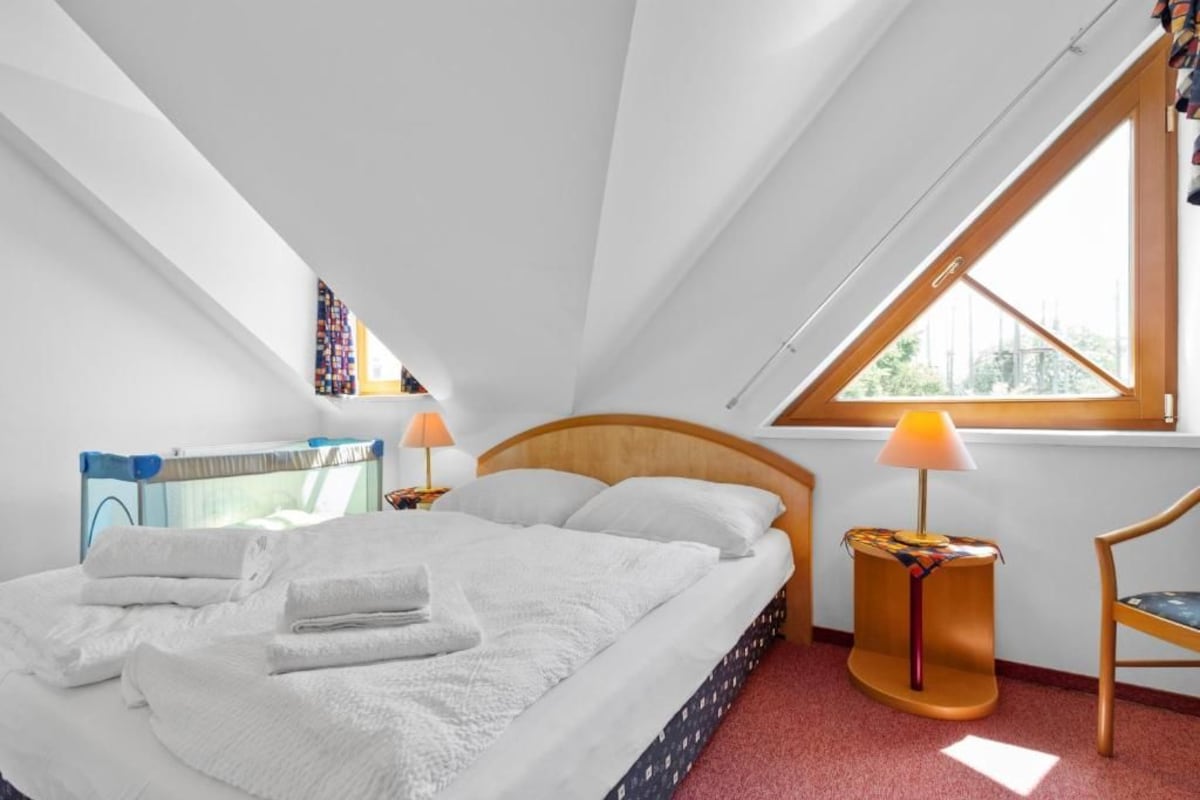 A bedroom with a large bed, two bedside lamps, a window, and a chair.