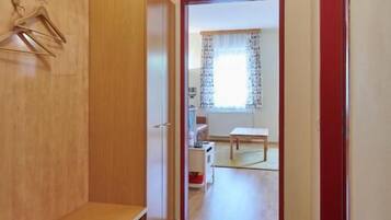 Een gang met een bank, een radiator en een deur die leidt naar een kamer met een raam.