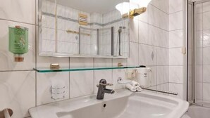 A bathroom with a white sink, a glass shelf, a mirror, and a shower area.