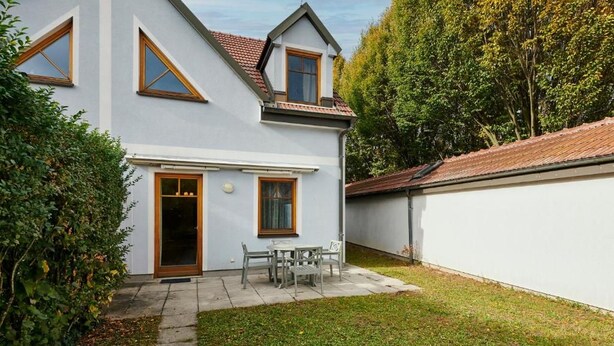 A two-story house with a front door, a small patio with a table and chairs, and a garden area.
