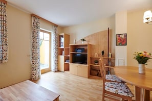 A living room with a wooden dining table, a TV on a wooden stand, and a bookshelf.