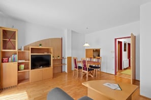 Una sala de estar moderna con televisor de pantalla plana, muebles de madera y un comedor con sillas y mesa.
