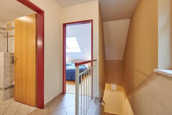 A hallway leading to a bedroom with a bed, a wooden door, and a white railing.