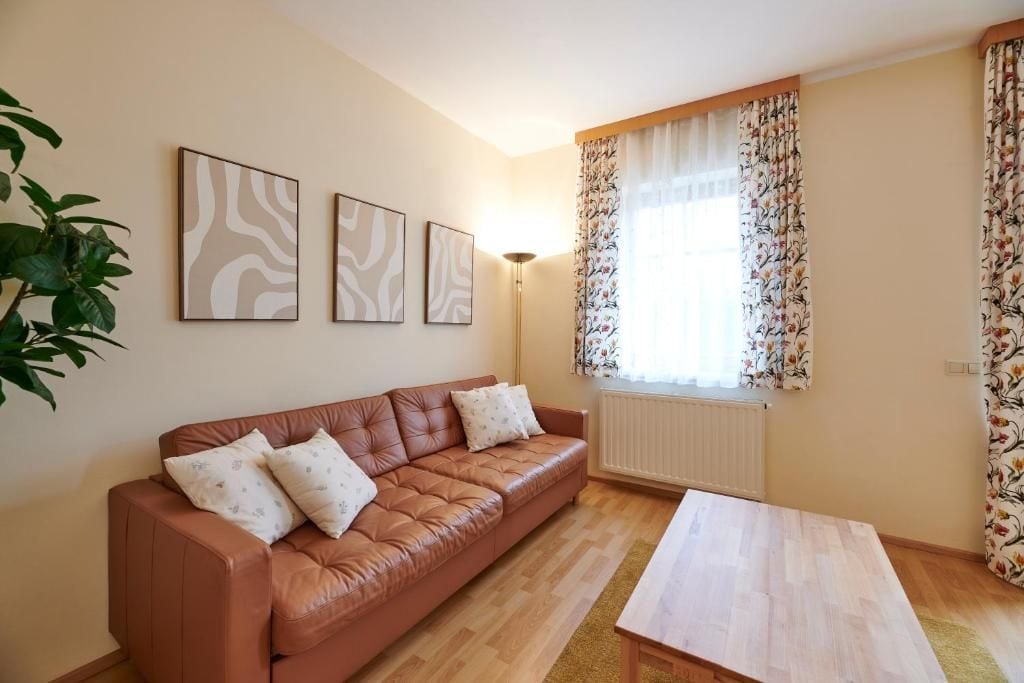 A living room with a brown leather sofa, a wooden coffee table, and a radiator. There are three framed abstract artworks on the wall.