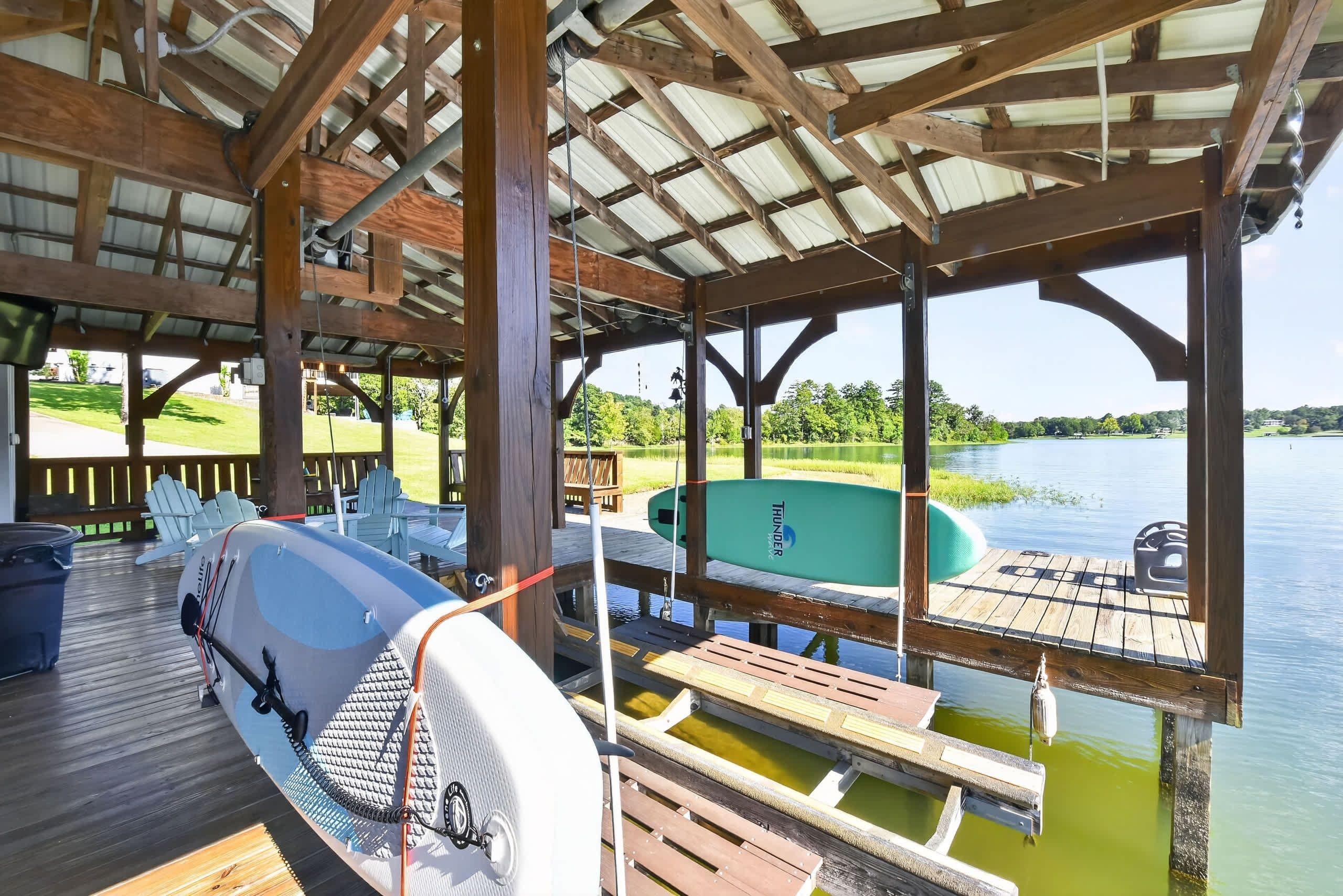 A covered dock area with a kayak and paddleboard, wooden deck, and a view of a lake.