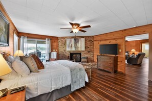 A bedroom with a bed, a ceiling fan, a fireplace, a TV, and a view of the outdoors. - Point of View l 3BR - Dock & Big Views (Northport)