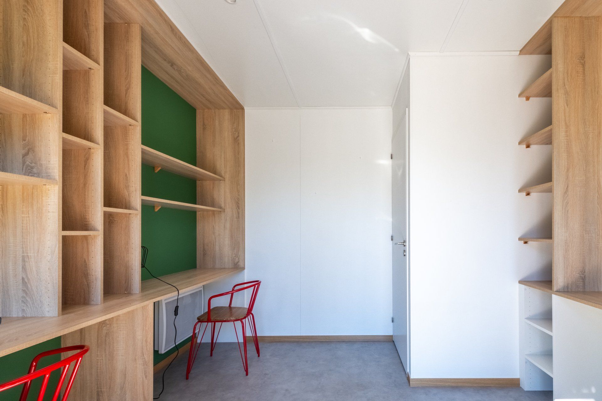 A room with built-in wooden shelving on the left, a green wall, a white door, and a red chair.