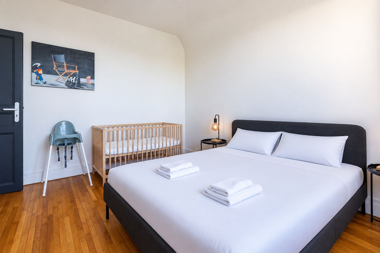 Une chambre à coucher avec un grand lit, un berceau, une chaise et un tableau accroché au mur.